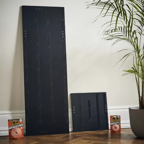 Nagy és kis dekorpanel hátulján elhelyezett Gorilla Mounting Tape XL csíkok, a padlón a csomagolással – kétoldalas extra erős rögzítés bemutatása
