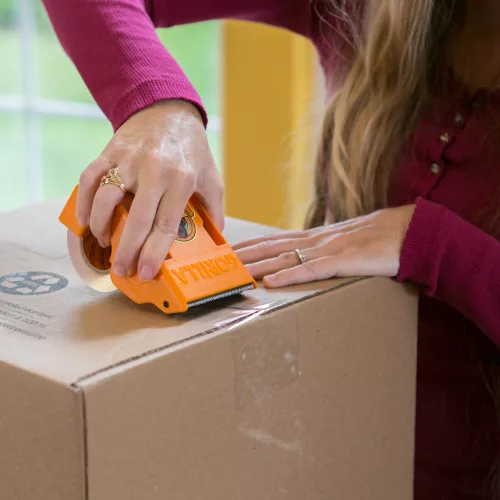 Nő Gorilla csomagolószalaggal zár le egy kartondobozt kézi adagoló segítségével