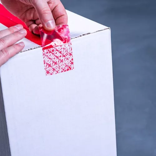 VOID plombáló szalag lehúzva, előtűnő „OPEN VOID” biztonsági minta dobozon