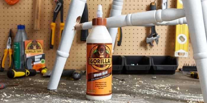 Gorilla Wood Glue faragasztó használat közben, fehér fa szék javításához műhelyben, szerszámokkal a háttérben.
